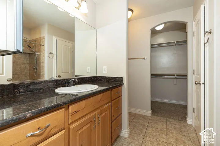 Vanity with a dark countertop and undermount sink, wood-finish cabinetry, and tiled flooring