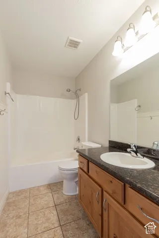 Bathroom featuring a bathtub with shower, tiled flooring, wood-finish vanity with an integrated sink, and dark stone-look countertop