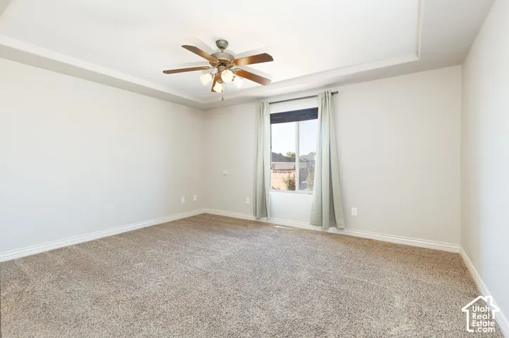 Tray ceiling with a ceiling fan, neutral carpet flooring, and a window with blinds