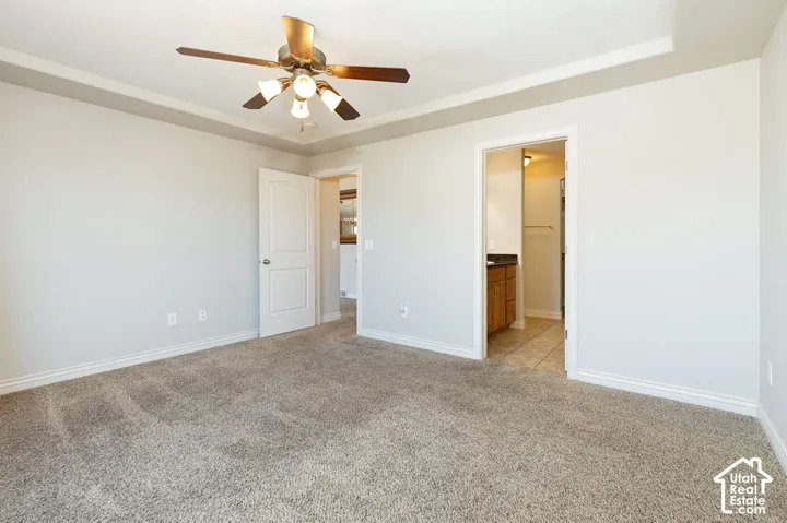 Recessed ceiling detail, ceiling fan with integrated lighting, neutral wall paint, carpet flooring, and a solid core interior door