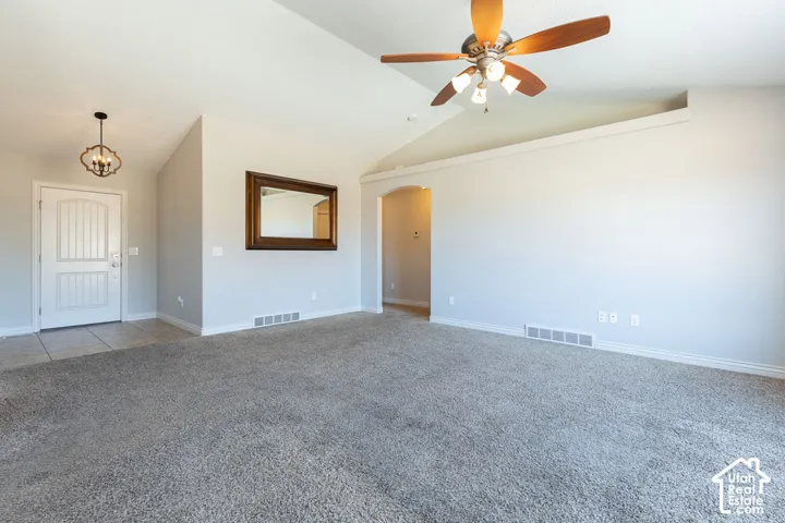 Vaulted ceiling, ceiling fan with integrated lighting, tiled entry, arched doorway, and carpeted flooring
