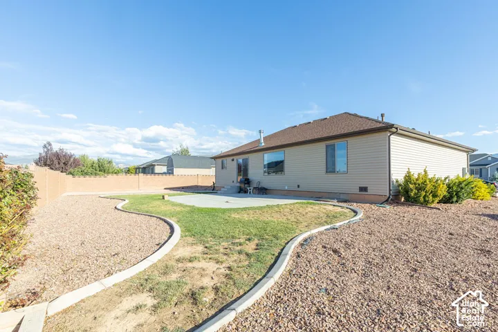 Expansive backyard featuring a concrete patio, a manicured lawn, gravel landscaping, and a privacy fence