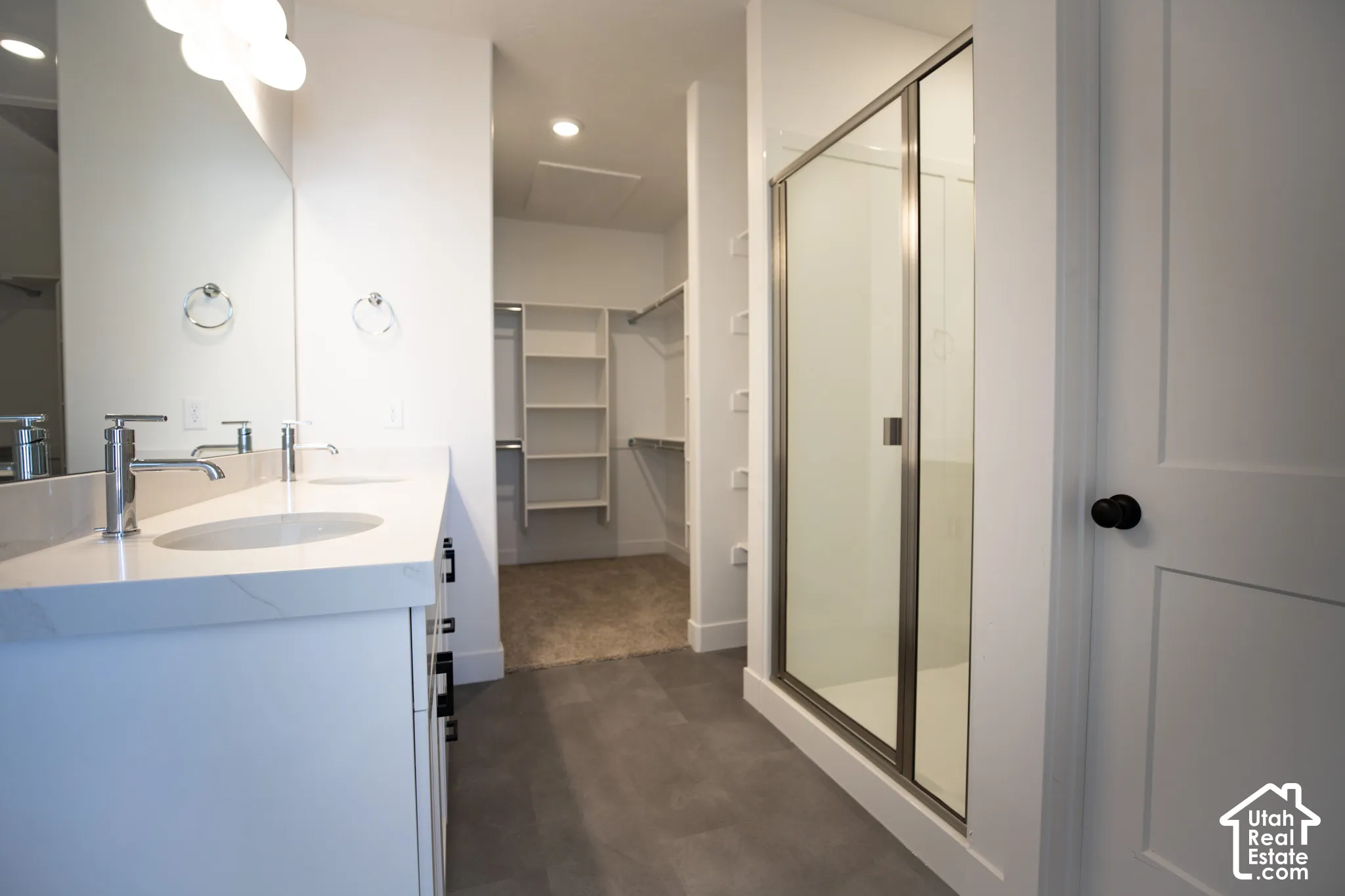 Primary bath with dual sinks, painted white wood cabinets, quartz slab countertops, large walk-in shower and spacious walk-in closet as part of primary suite.