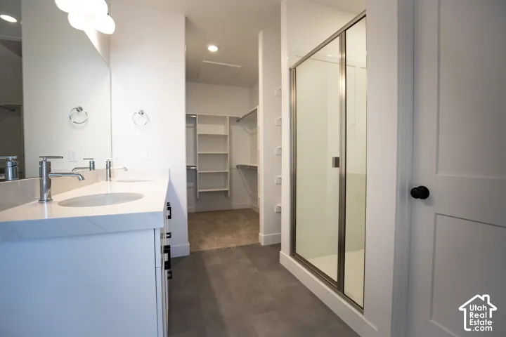 Primary bath with dual sinks, painted white wood cabinets, quartz slab countertops, large walk-in shower and spacious walk-in closet as part of primary suite.