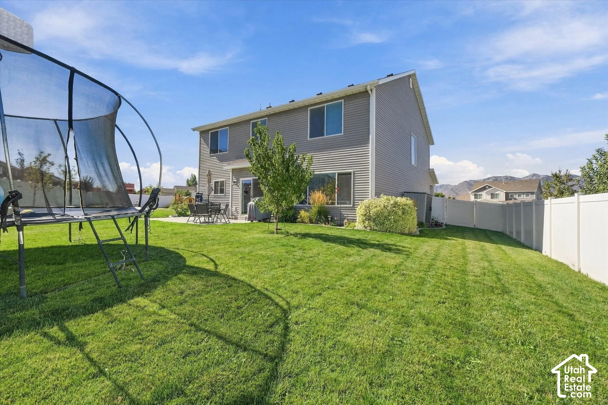 Expansive backyard featuring a manicured lawn, established landscaping, and a privacy fence