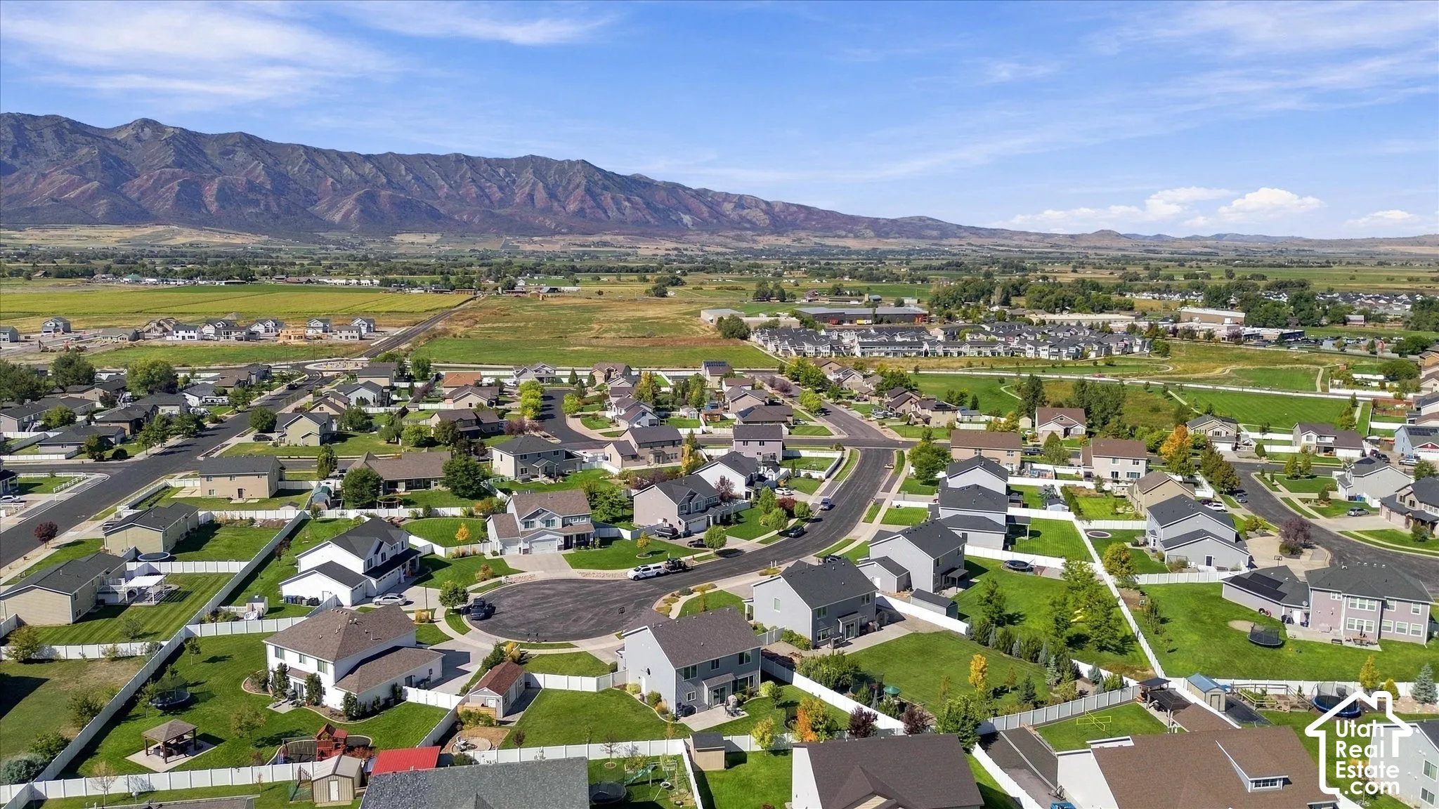 Residential neighborhood with diverse home styles, paved streets, and green spaces, set against a backdrop of distant mountains