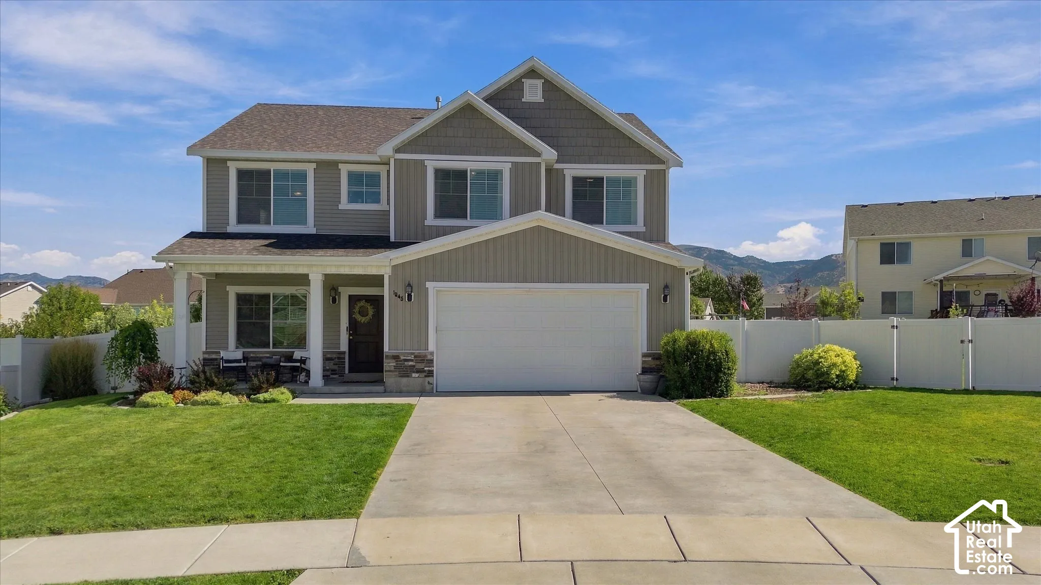 Two-story residence featuring a covered front porch, attached garage, concrete driveway, and a manicured lawn