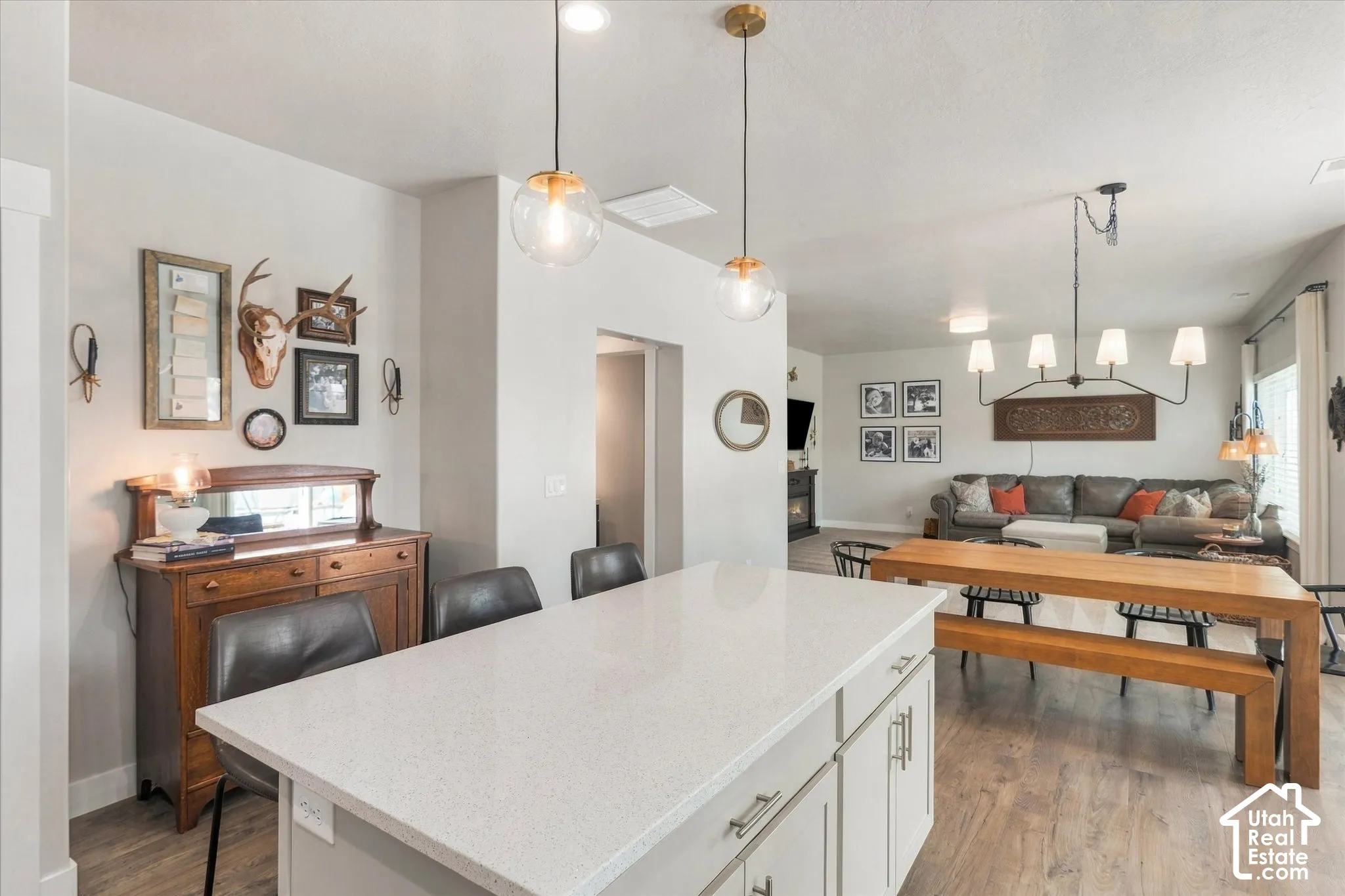Kitchen island with a light-toned countertop, two pendant light fixtures, wood-finish flooring, and a formal dining area with a linear chandelier