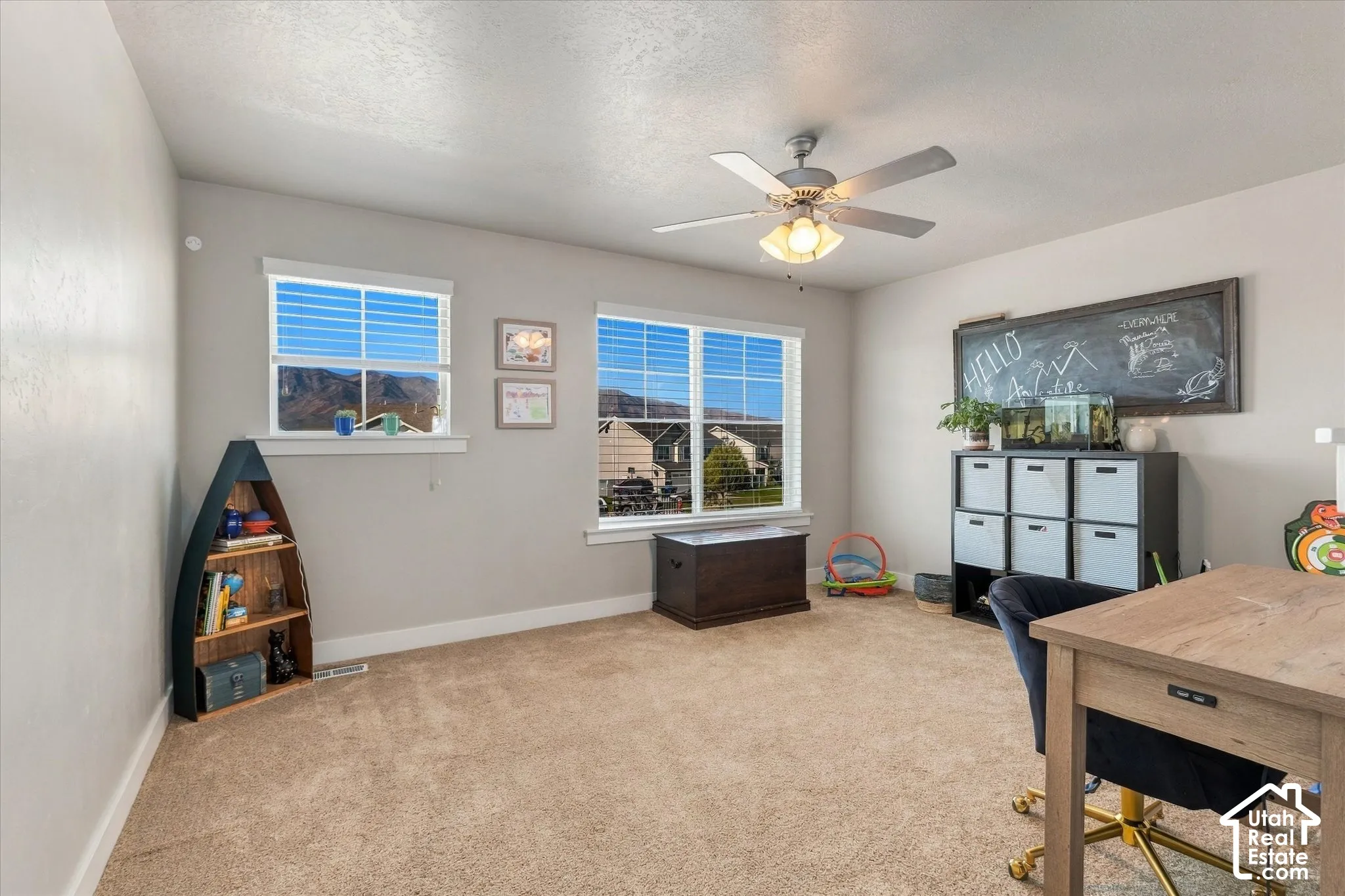 Neutral wall color, carpet flooring, windows with blinds, and a ceiling fan with integrated lighting