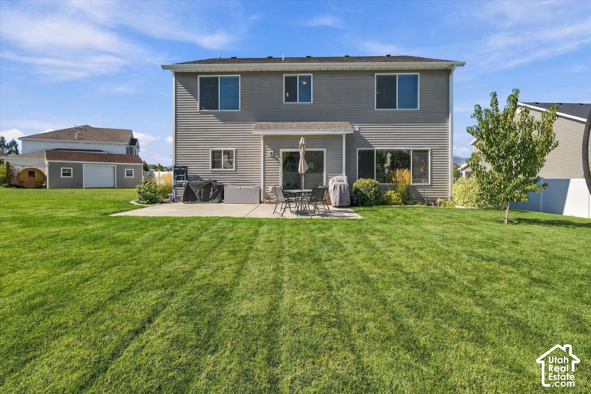 Expansive green lawn with a concrete patio, mature landscaping, and a two-story residence featuring horizontal siding