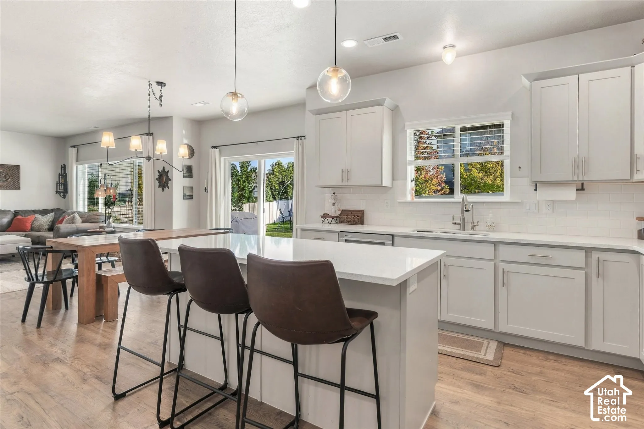 Kitchen featuring light-toned cabinetry, light countertops, subway tile backsplash, stainless steel sink with a gooseneck faucet, and wood-finish flooring