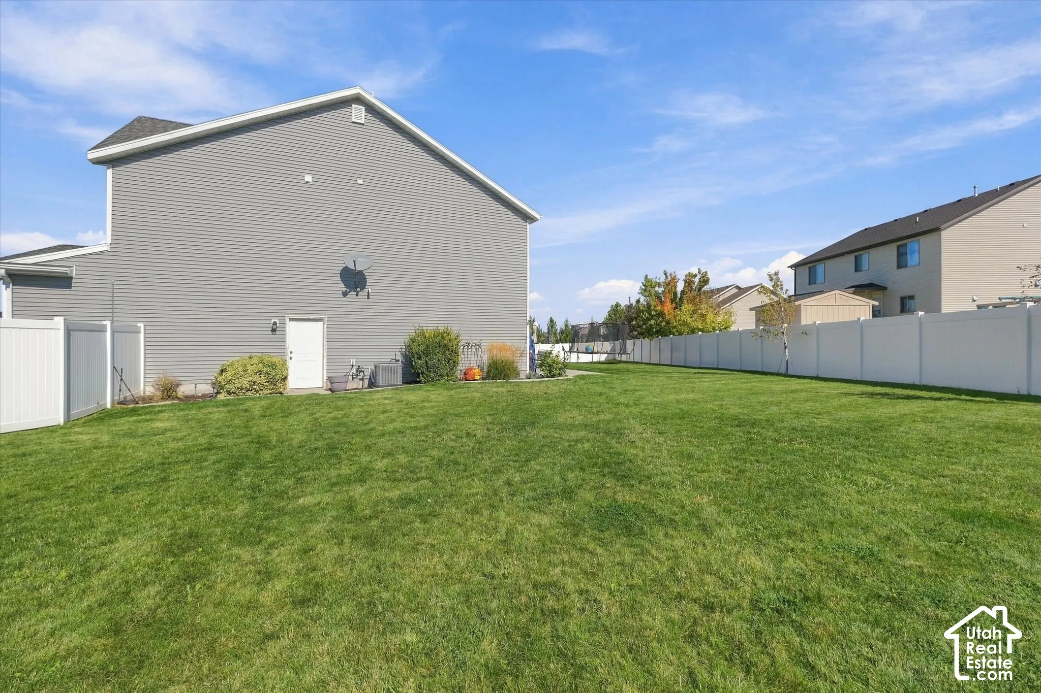 Expansive grassy yard with white vinyl fencing and a side-entry door