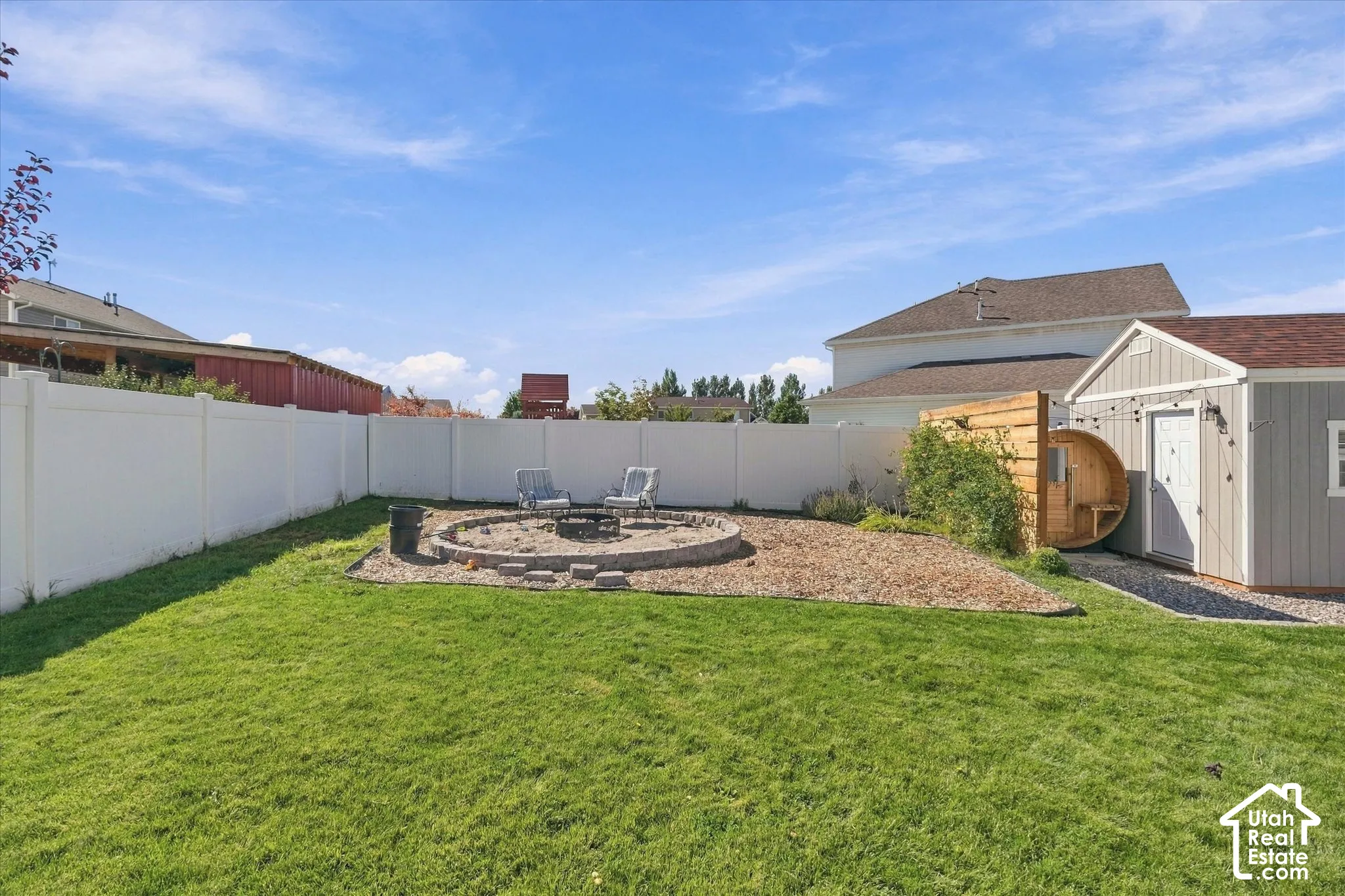 Expansive lawn with a white privacy fence, stone fire pit, wood-sided shed, and a barrel sauna