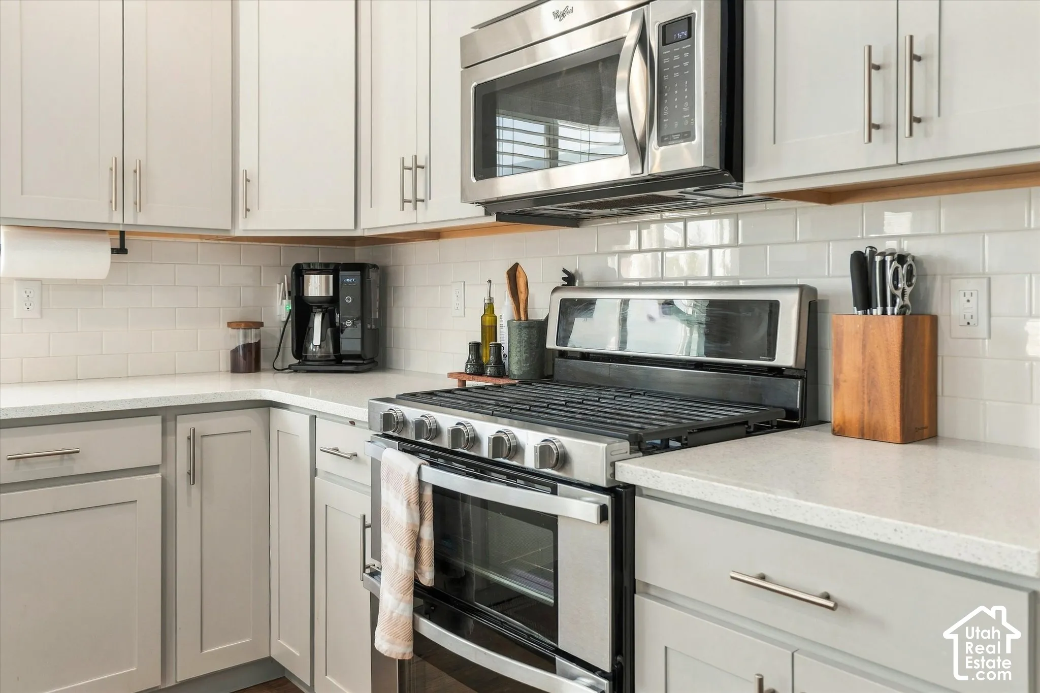 White subway tile backsplash, light grey cabinetry with brushed nickel hardware, stainless steel gas range, stainless steel microwave, and light-toned countertops