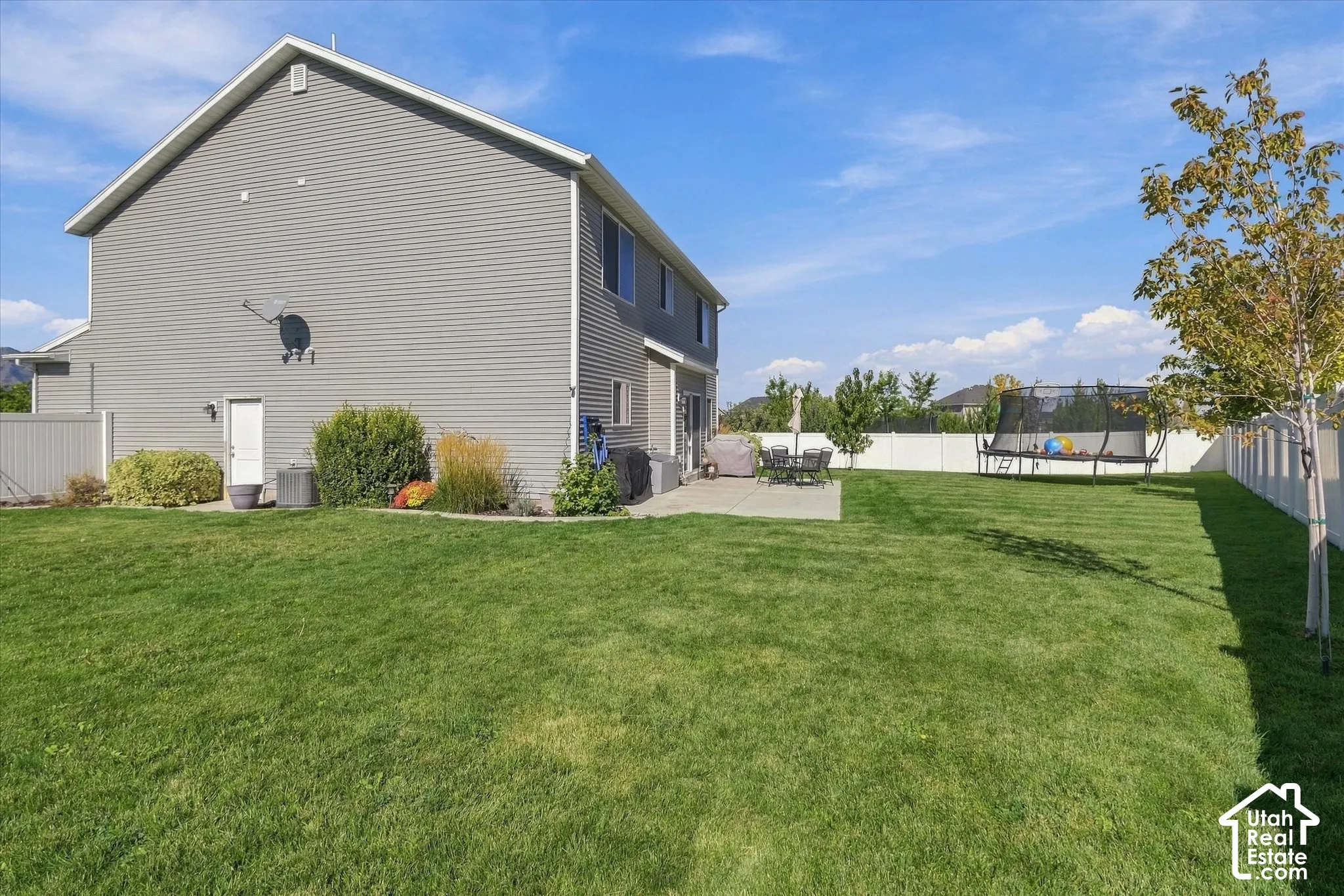 Expansive backyard featuring a manicured lawn, established landscaping, privacy fencing, and a concrete patio
