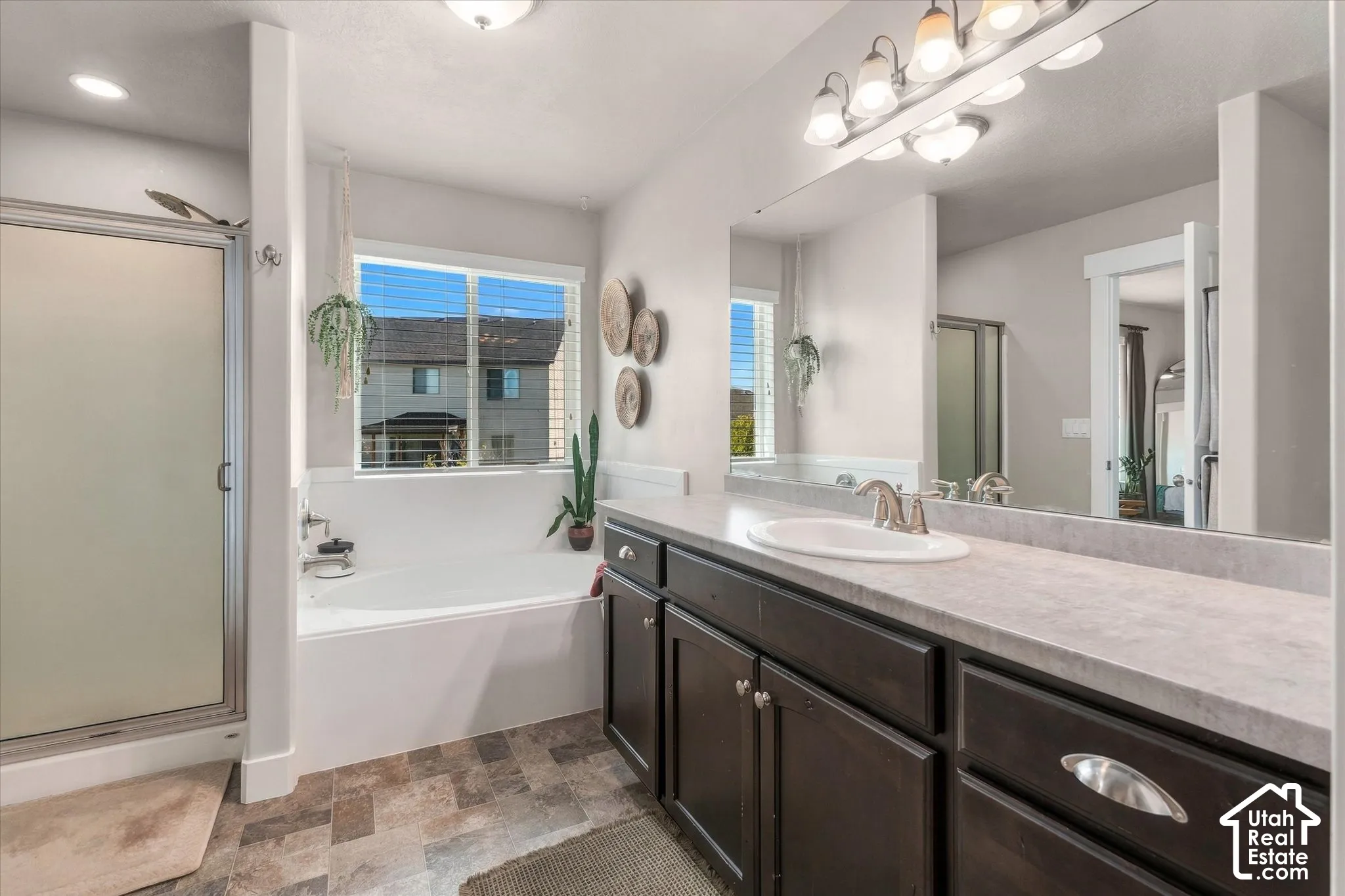 Built-in bathtub with a window above, separate enclosed shower with frosted glass, wood-finish vanity with an integrated sink, and an expansive mirror