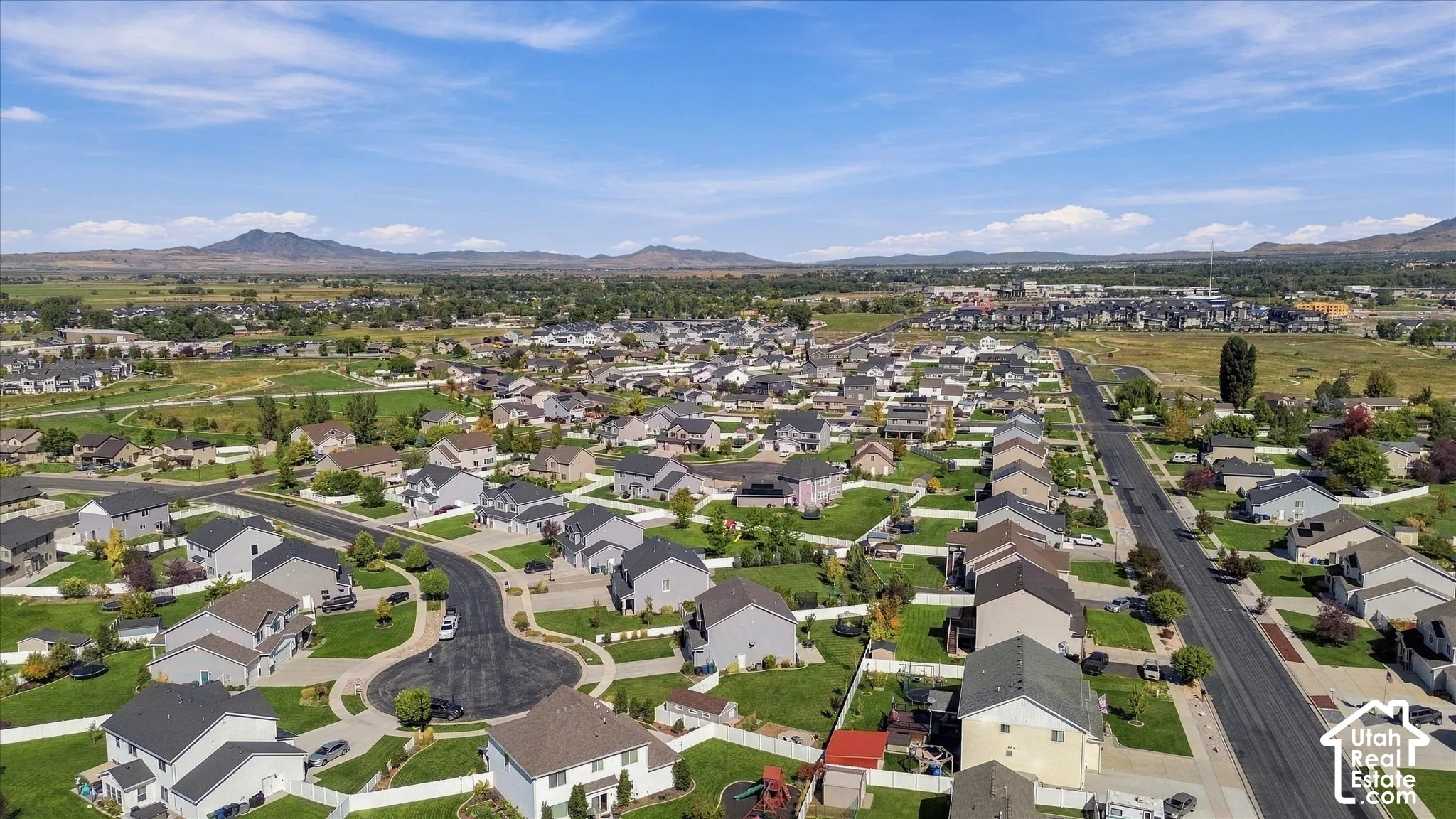 Residential development featuring multiple single-family homes with pitched roofs, expansive green spaces, and paved streets with cul-de-sacs