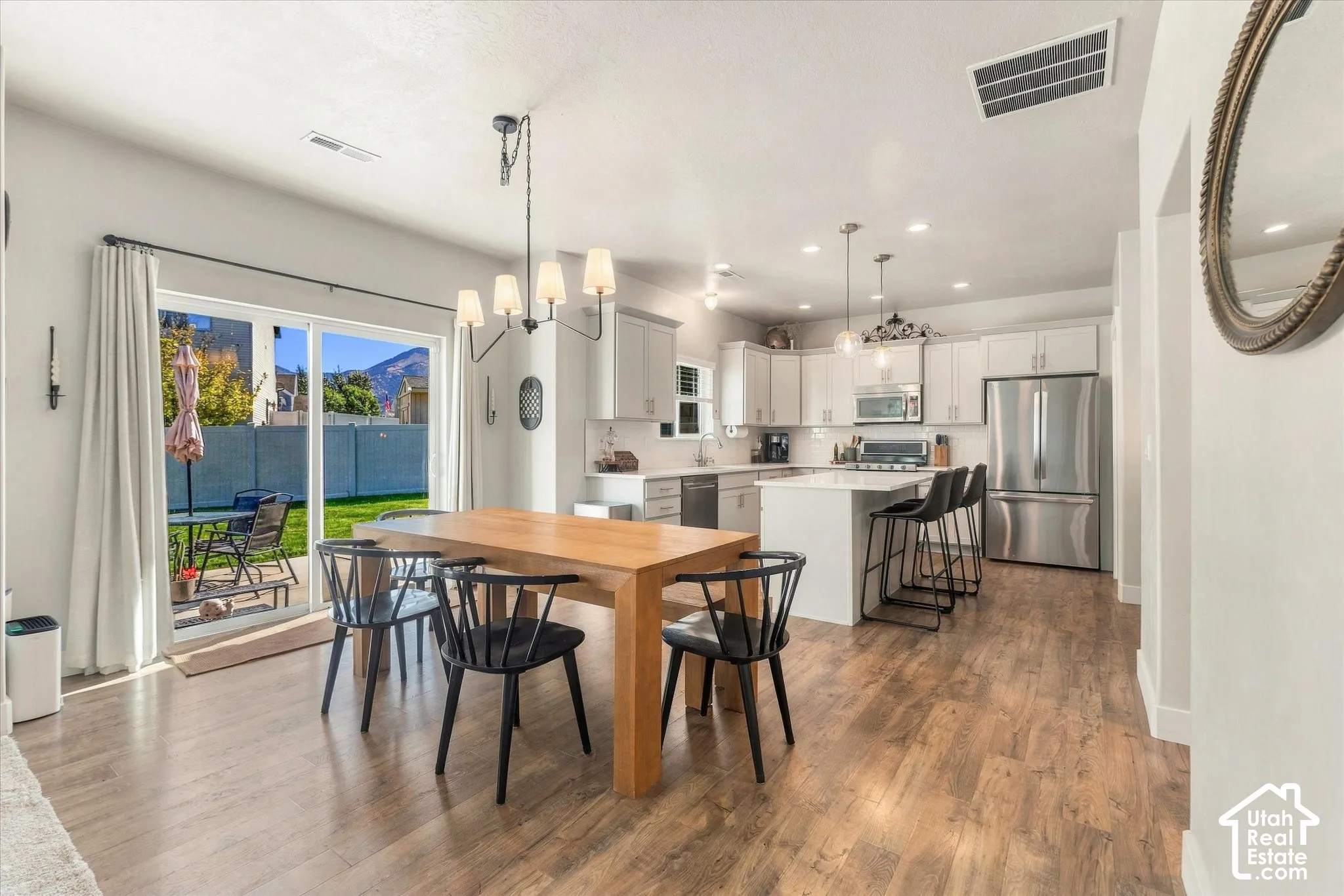 Wood-finish flooring, white cabinetry, stainless steel appliances, central kitchen island, and sliding glass door access to the backyard