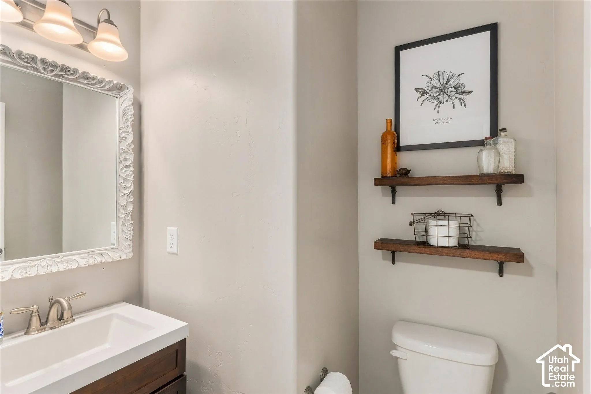 White framed mirror with ornate detailing, a single basin vanity with a wood-finish cabinet, and a two-tiered floating shelf system