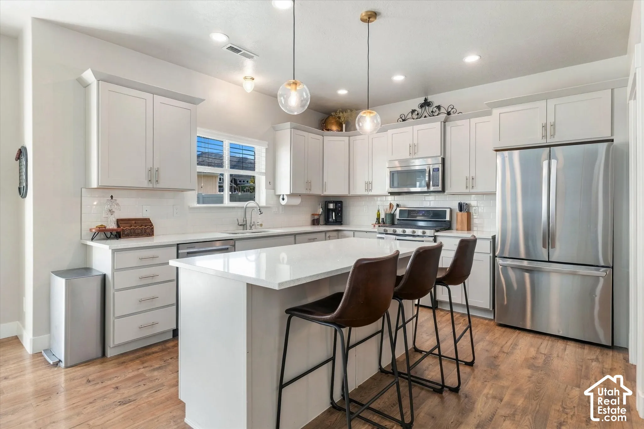 White shaker cabinetry, stainless steel appliances, wood-finish flooring, recessed lighting, and a kitchen island with a quartz countertop