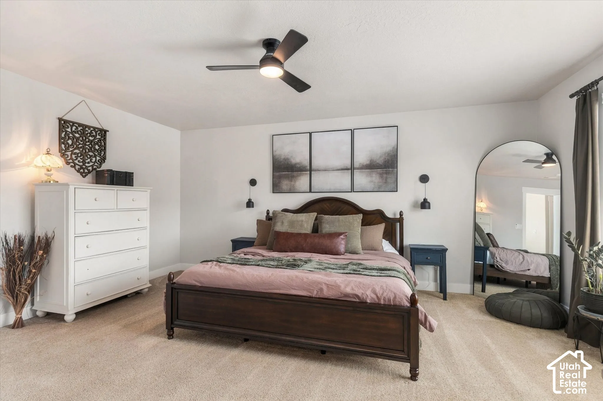 Plush carpet flooring, ceiling fan with integrated lighting, dark wood bed frame, white walls, and dark window treatments