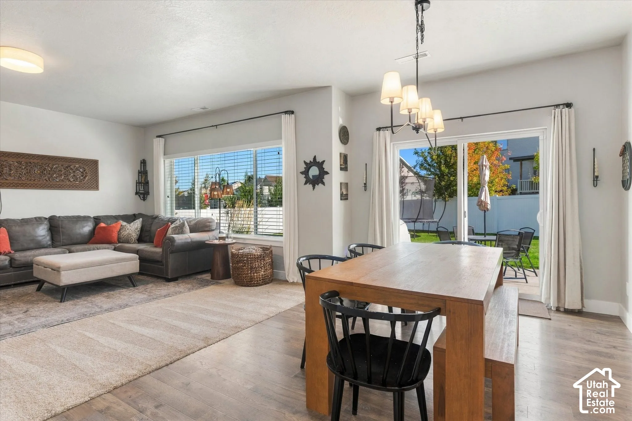Open-concept living area with wood-finish flooring, a contemporary chandelier, and large windows with horizontal blinds