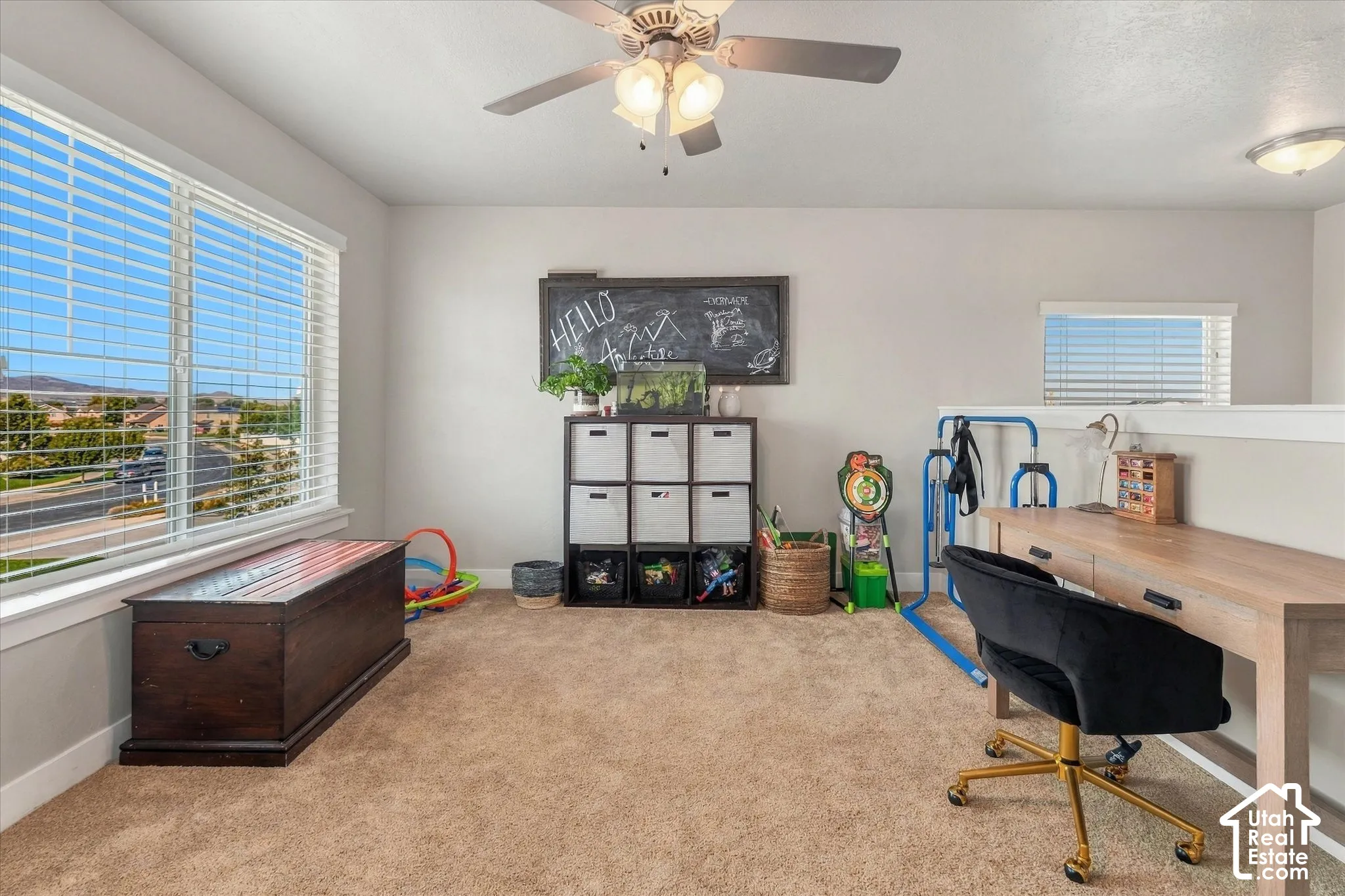 Carpeted room with a ceiling fan, dual windows, and a built-in half-wall