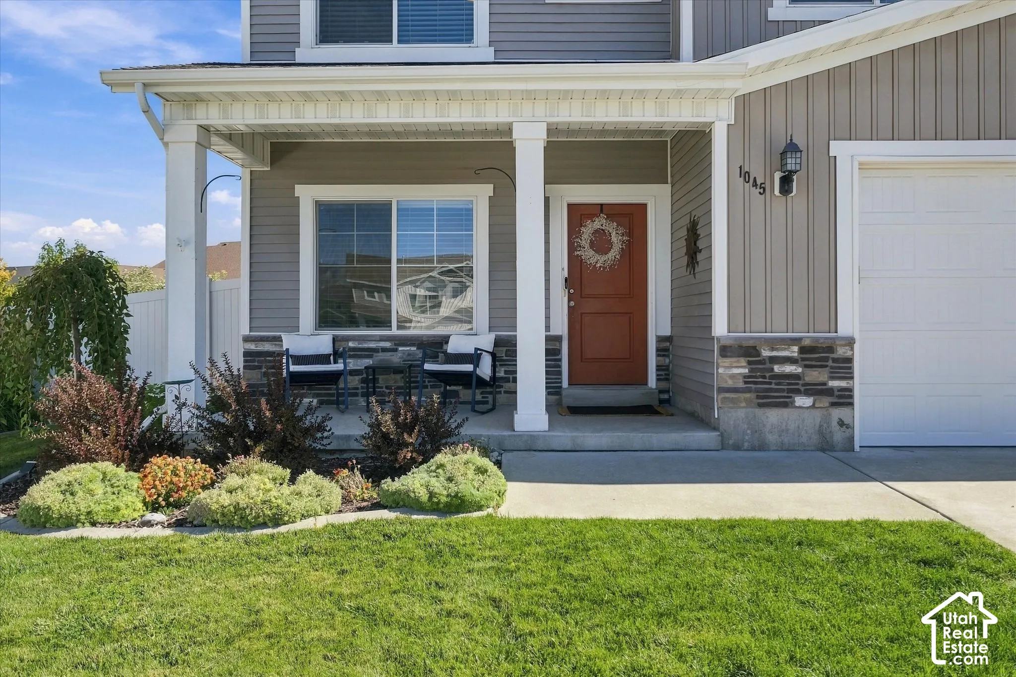 Covered front porch with white columns, horizontal and vertical siding, stone accent detailing, and an attached garage
