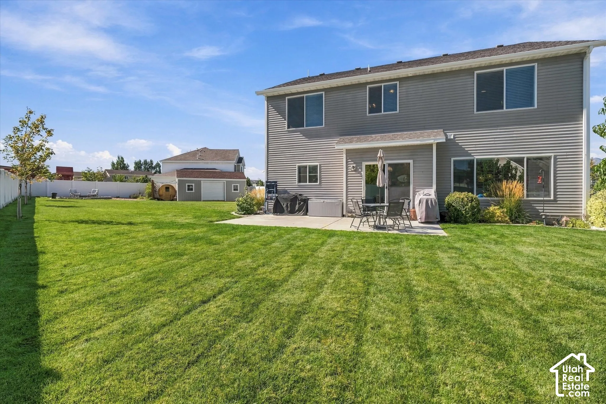 Expansive green lawn, white fence, rear patio, and a separate storage shed