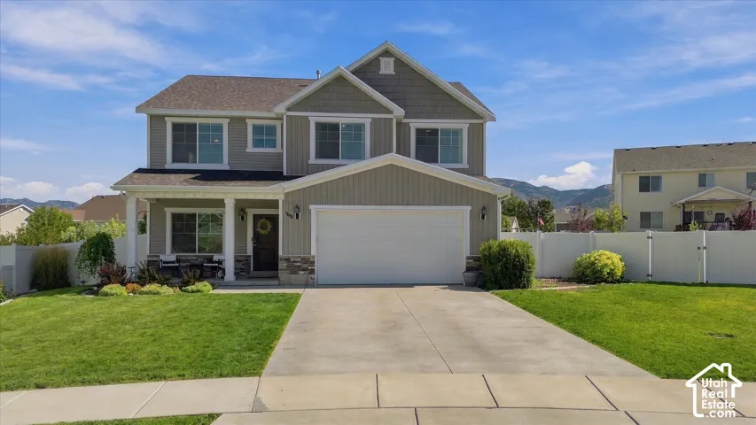 Two-story residence featuring a covered front porch, attached garage, concrete driveway, and a manicured lawn