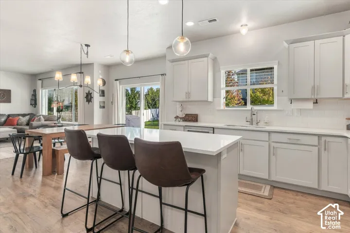 Kitchen featuring light-toned cabinetry, light countertops, subway tile backsplash, stainless steel sink with a gooseneck faucet, and wood-finish flooring