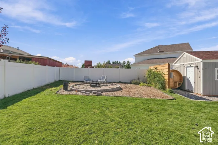 Expansive lawn with a white privacy fence, stone fire pit, wood-sided shed, and a barrel sauna