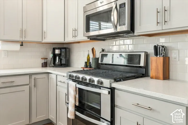 White subway tile backsplash, light grey cabinetry with brushed nickel hardware, stainless steel gas range, stainless steel microwave, and light-toned countertops