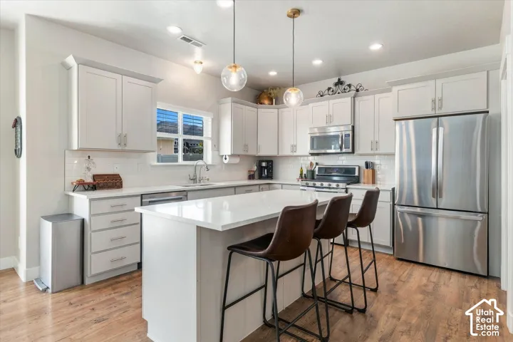 White shaker cabinetry, stainless steel appliances, wood-finish flooring, recessed lighting, and a kitchen island with a quartz countertop