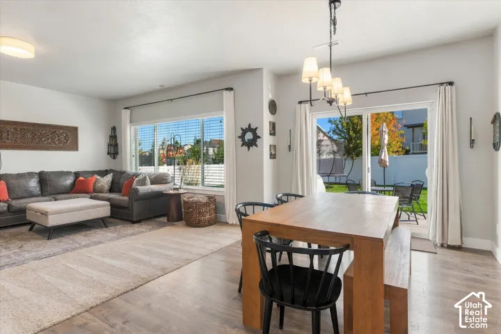Open-concept living area with wood-finish flooring, a contemporary chandelier, and large windows with horizontal blinds