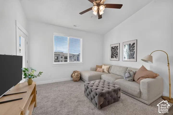 Angled ceiling, wood-finish ceiling fan with integrated lighting, window with blinds, light gray carpeting, and white trim throughout