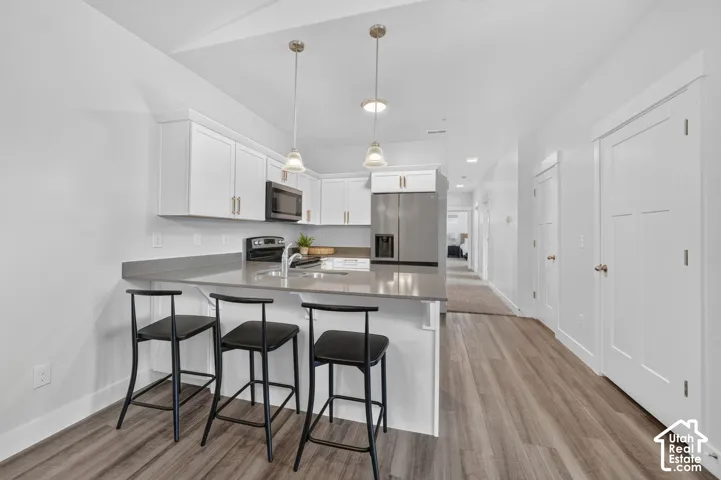 Kitchen featuring stainless steel appliances, white cabinetry, a large kitchen island with counter seating, and wood-finish flooring