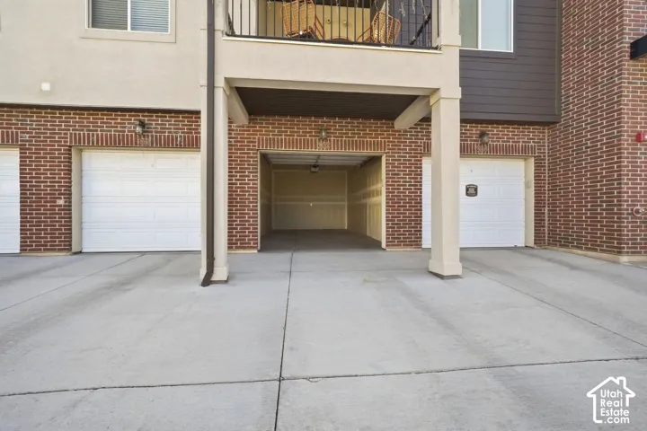 Brick exterior with a ground-level garage, concrete driveway, and an upper-level balcony