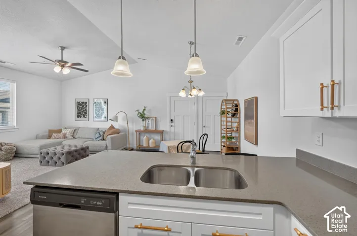 Kitchen island with dual stainless steel sink, gray countertop, white cabinetry with gold-toned hardware, and integrated dishwasher