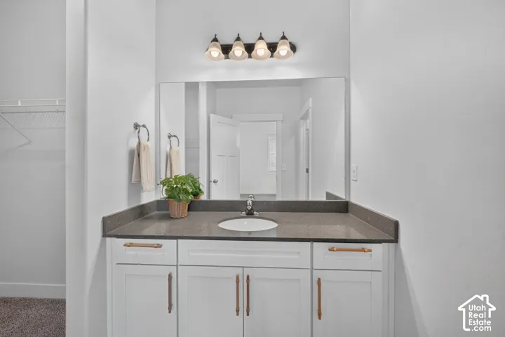 White vanity with a single basin sink, a dark countertop, and a large mirror