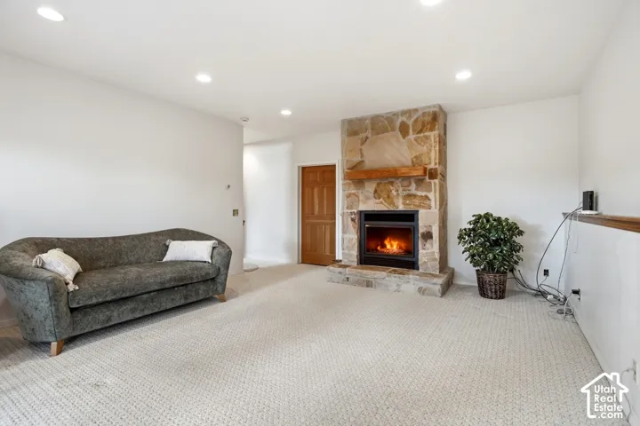 Living area with a stone-clad fireplace and wood mantel, recessed lighting, and neutral carpeting