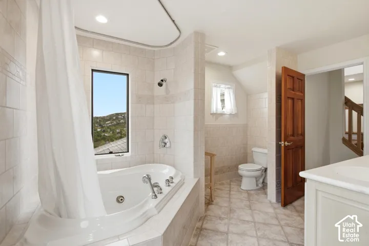 Soaking tub with integrated jets, tiled shower surround, recessed lighting, and a single vanity with an integrated sink