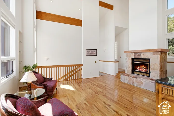Soaring ceilings with exposed wood beams, stone-faced fireplace with wood mantel, wood-finish flooring, and multiple large windows