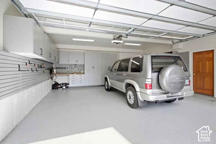 Garage featuring overhead cabinetry, slatwall storage system, built-in workbench, overhead lighting, and a wood-paneled door