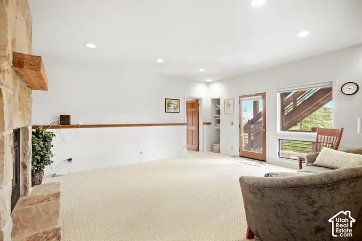 Stone-clad fireplace with a wood mantel, recessed lighting, wood-finish doors, built-in shelving, and large windows