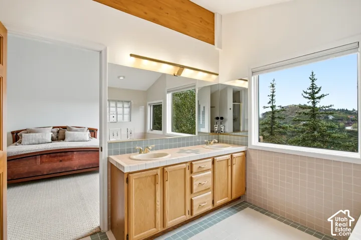 Dual vanity with light wood cabinetry, tiled countertop, and large mirror