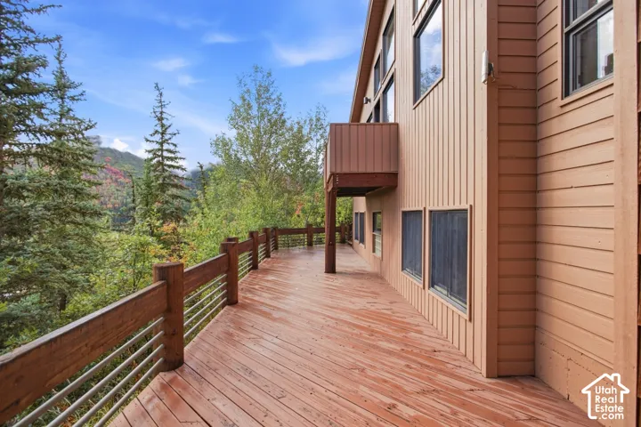 Expansive wood-finish deck with cable railing, featuring direct access to a private balcony and a tan siding exterior