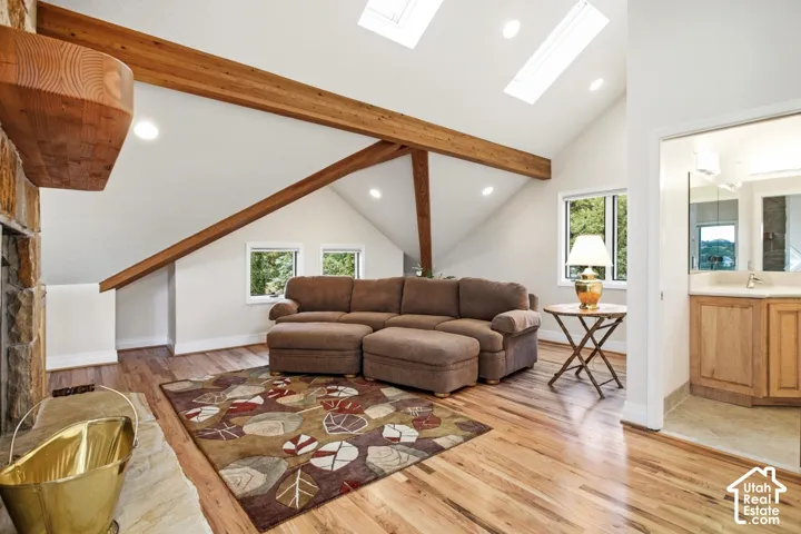 Vaulted ceiling with exposed wood beams, skylights, recessed lighting, wood-finish flooring, and a stone fireplace