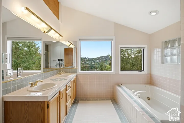 Bathroom featuring a dual vanity, built-in soaking tub, tiled floor, and multiple windows