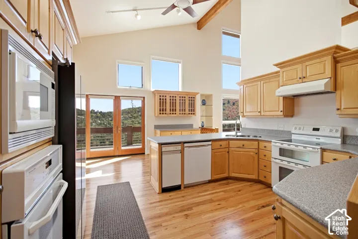 Kitchen featuring wood-finish flooring, light wood cabinetry, white appliances, and a central island